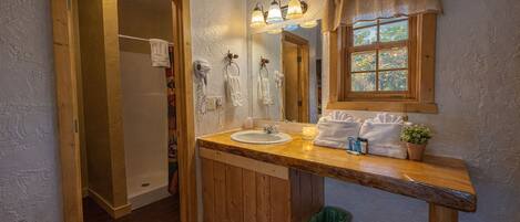 A bathroom with a wooden vanity, a sink, a mirror, and a window with curtains.