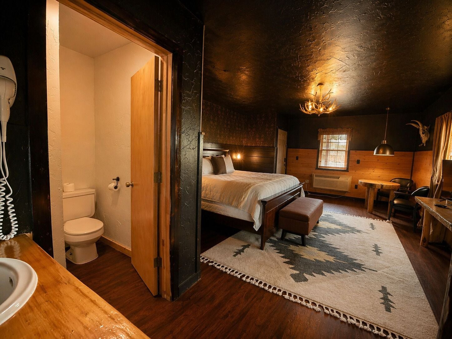 A bedroom with a bed, a wooden bench, a rug, a desk, and a chair.