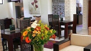 A living room with a glass coffee table, wicker chairs, and a sofa. There is a vase with flowers on the coffee table. - Rustenburg Boutique Hotel (Rustenburg)