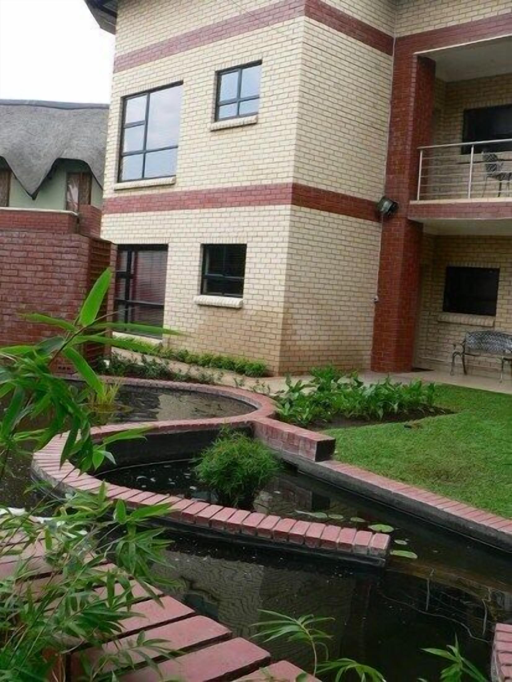 Un edificio de dos plantas con fachada de ladrillo, un pequeño jardín con un estanque y un balcón con mobiliario exterior.