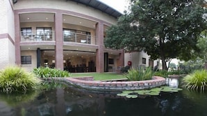 A multi-story building with a courtyard featuring a pond with lily pads and surrounding greenery. - Rustenburg Boutique Hotel (Rustenburg)