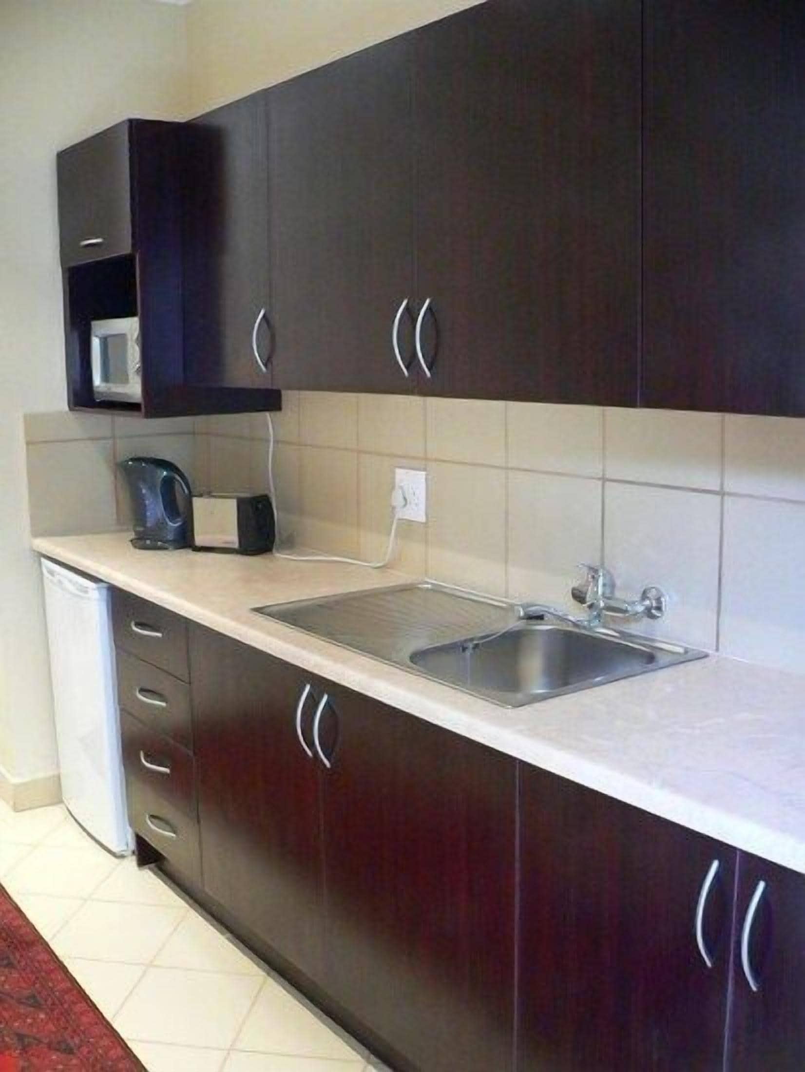 A modern kitchen with dark cabinetry, a stainless steel sink, and a microwave.