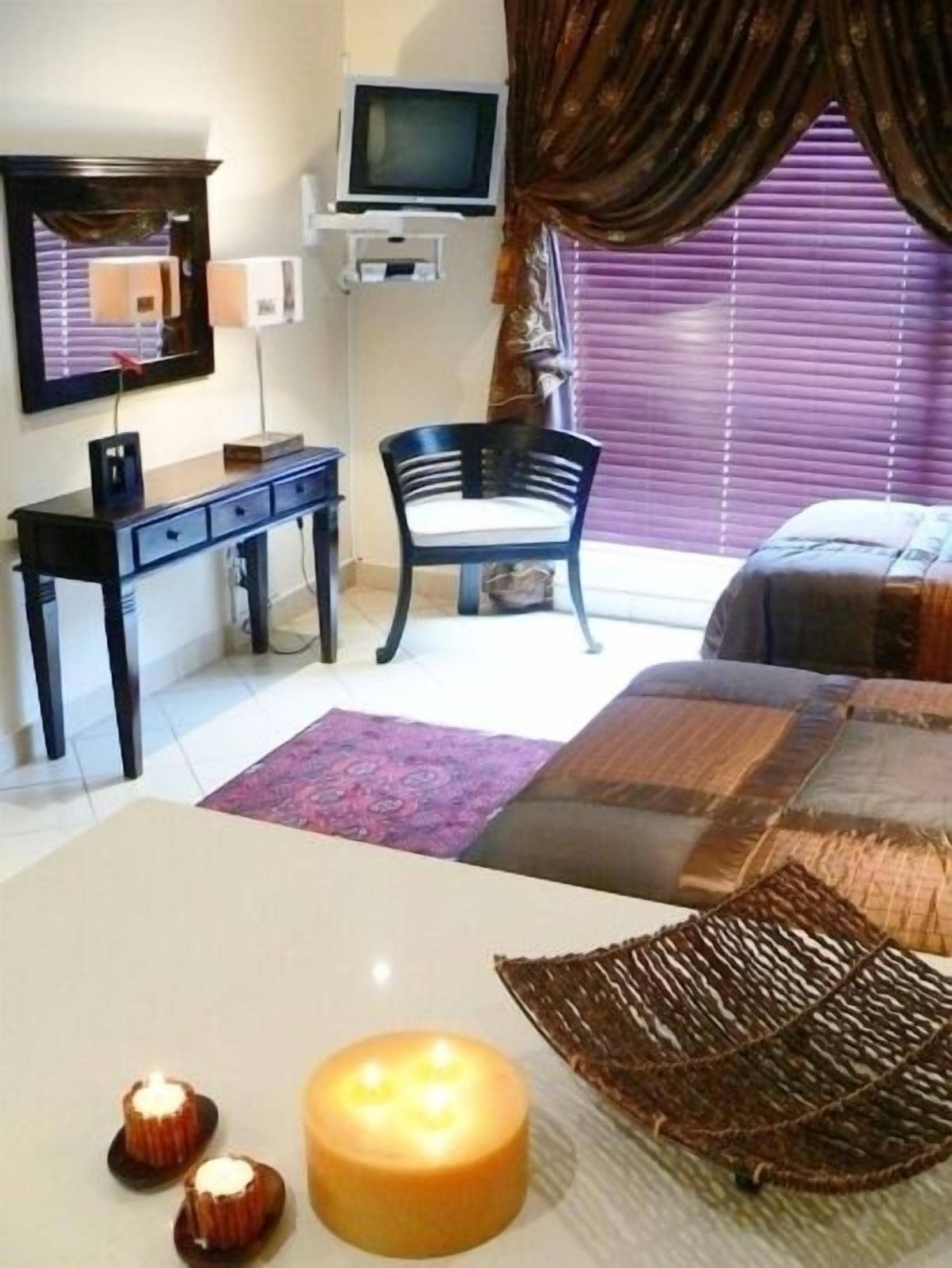 A bedroom with a bed, a desk, a chair, a TV, and a window with blinds.