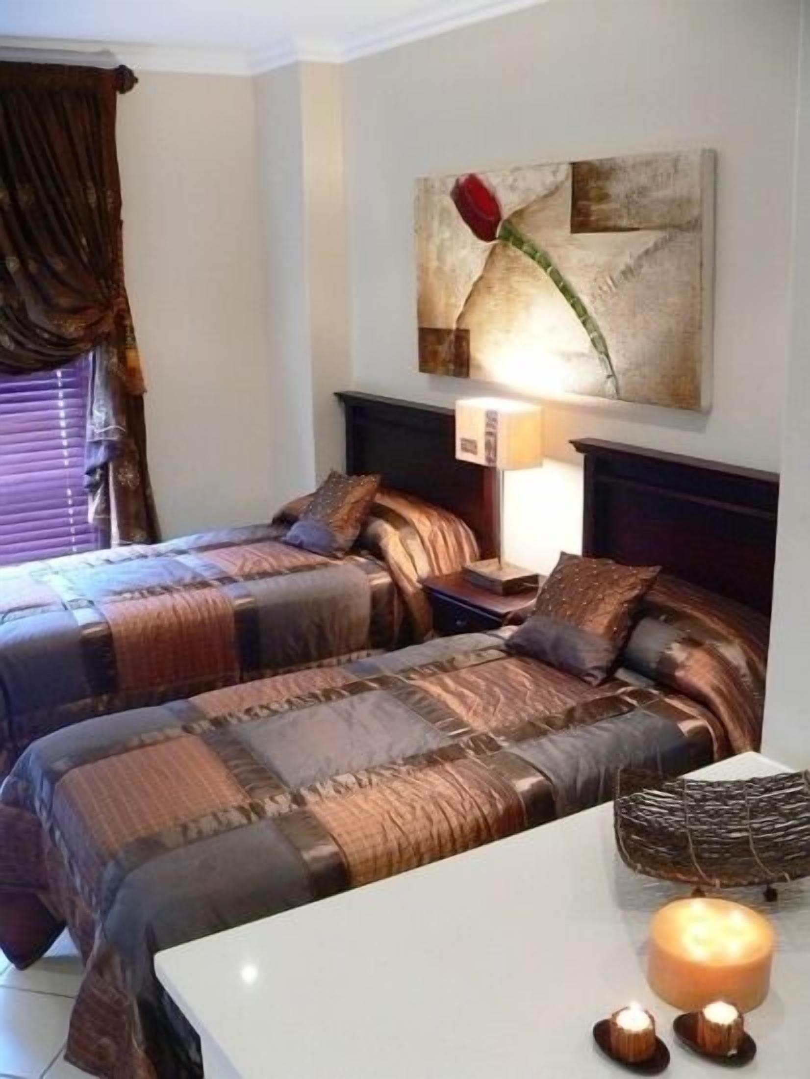 Une chambre d’hôtel avec deux lits, une table de chevet, une lampe, un tableau décoratif au mur et une bougie sur la table.