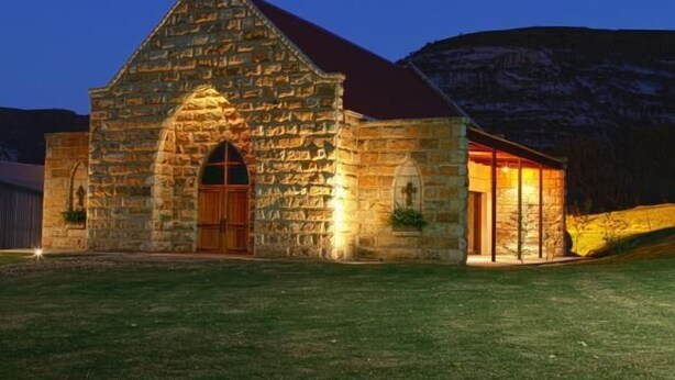 A stone building with a red roof, a wooden door, and a lit interior. - Oranje Gasteplaas Maloti Route (Fouriesburg)