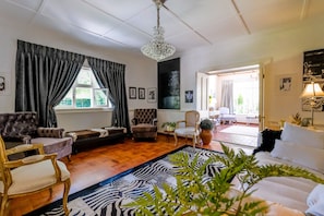 A spacious living room with a chandelier, a zebra-patterned rug, and a variety of seating options including a sofa, armchairs, and a tufted leather couch.