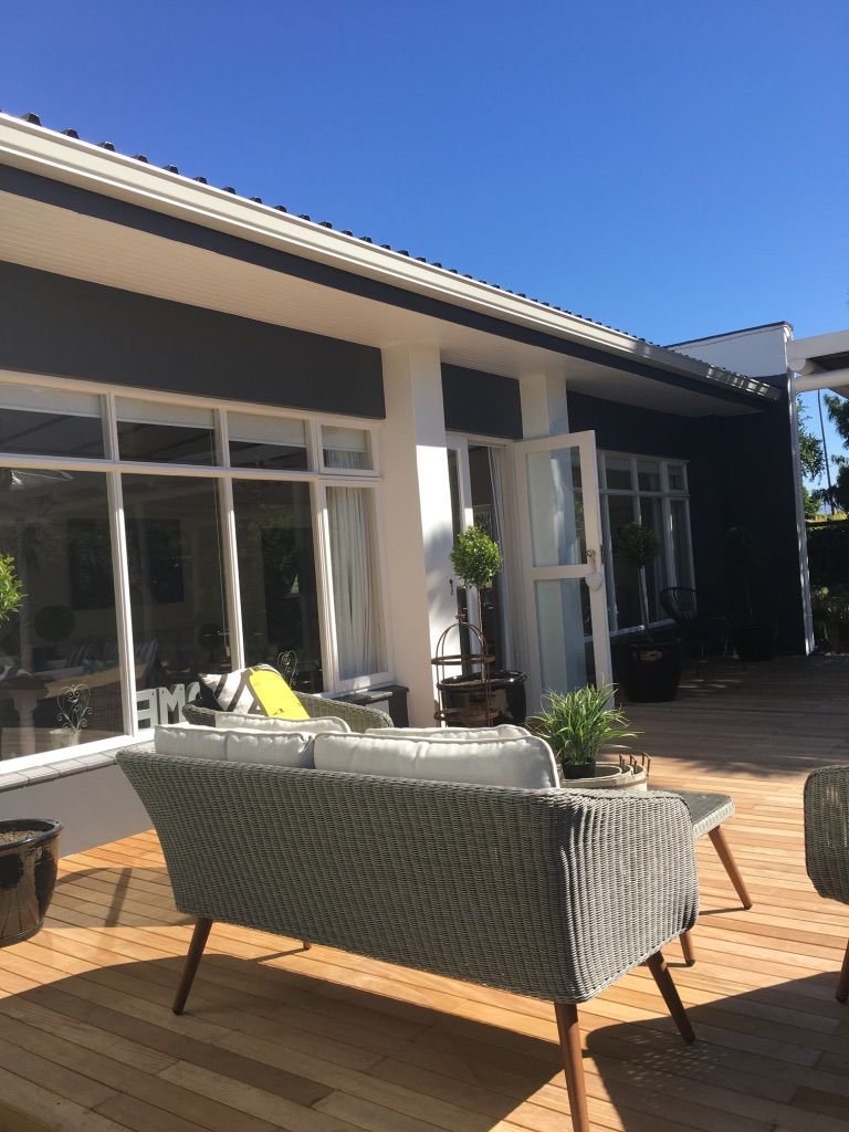 Un espacio de patio al aire libre con mobiliario de mimbre, una terraza de madera y un edificio moderno con grandes ventanales.