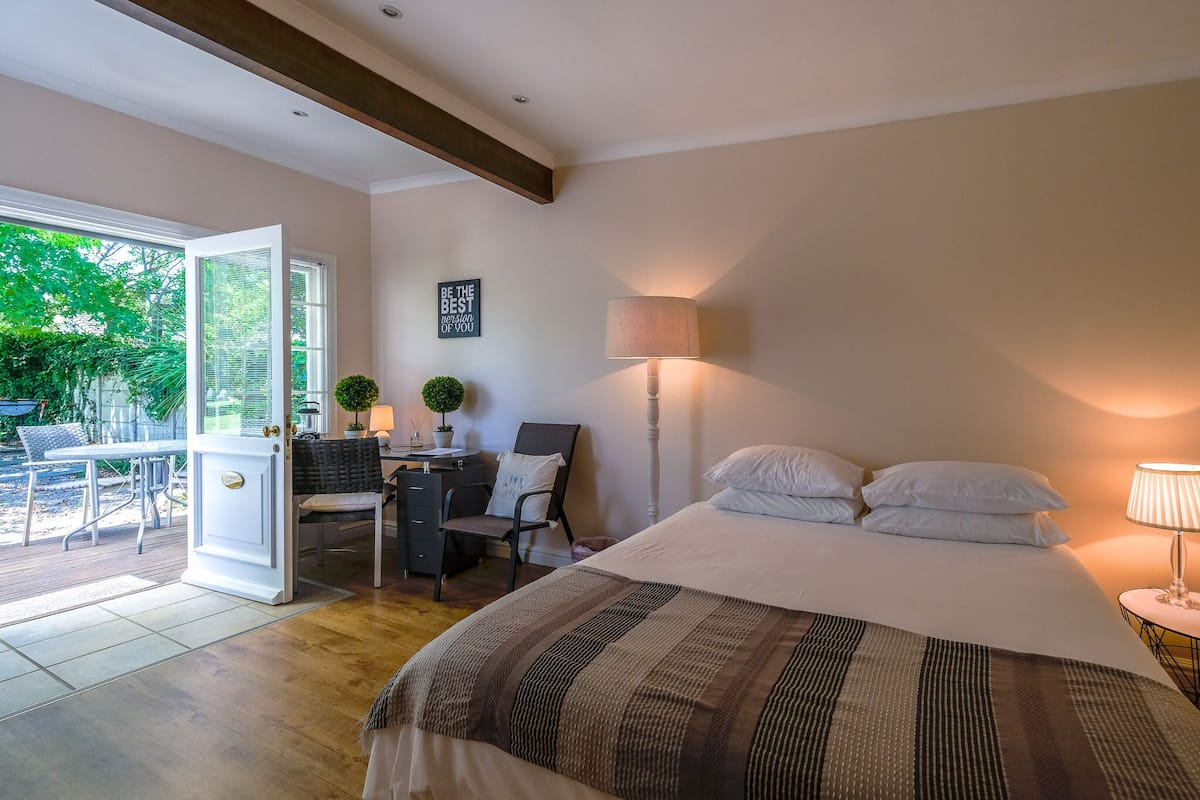 Un dormitorio con cama, lámpara de noche, escritorio, silla y vistas al exterior.