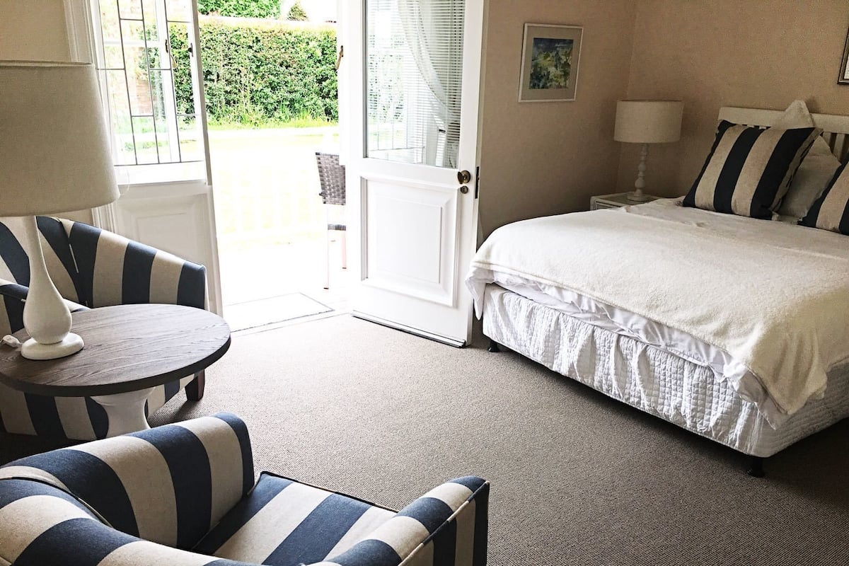 Habitación de hotel con una cama, una silla, una mesita y una puerta que da a un balcón.