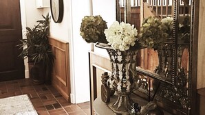 A hallway with a large mirror, a potted plant, and a vase with flowers. - Oude Berg Guesthouse (George)