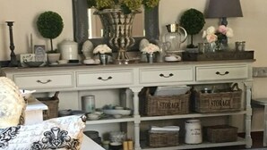 A room with a white dresser, wicker baskets labeled 'STORAGE', and a potted plant with purple flowers. - Oude Berg Guesthouse (George)