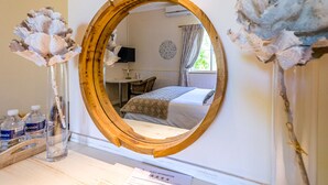 A hotel room with a wooden-framed mirror, a bed with a patterned bedspread, a desk with a chair, and a window with curtains. - Oude Berg Guesthouse (George)