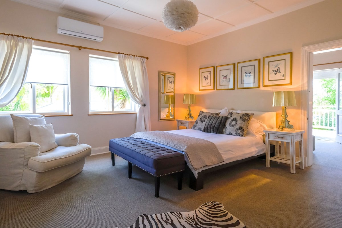 Un dormitorio con cama, un banco, una silla y una pequeña mesa con lámparas.