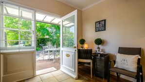 An open door leading to a patio with a table and chairs, a small lamp, and a chair with a cushion. - Oude Berg Guesthouse (George)