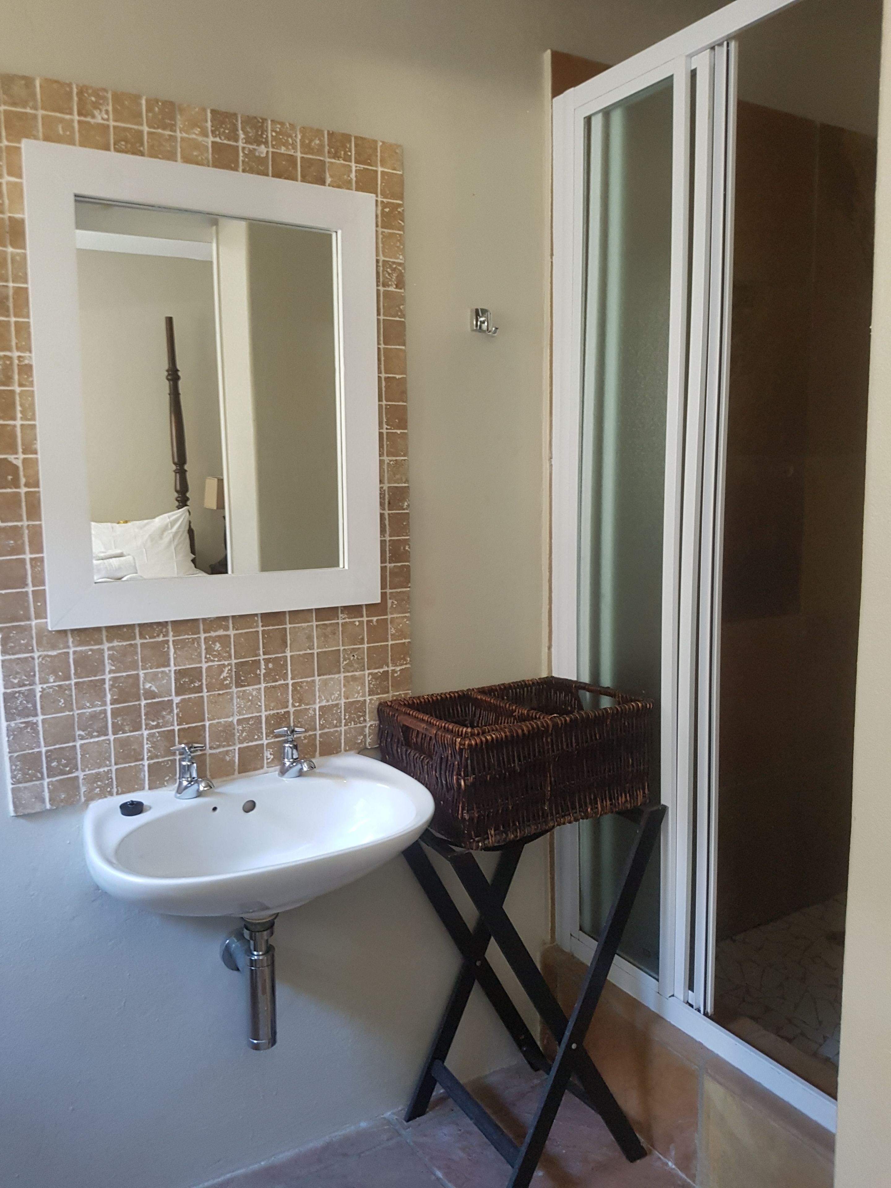 A bathroom with a white sink, a mirror, and a wicker basket on a black stand.