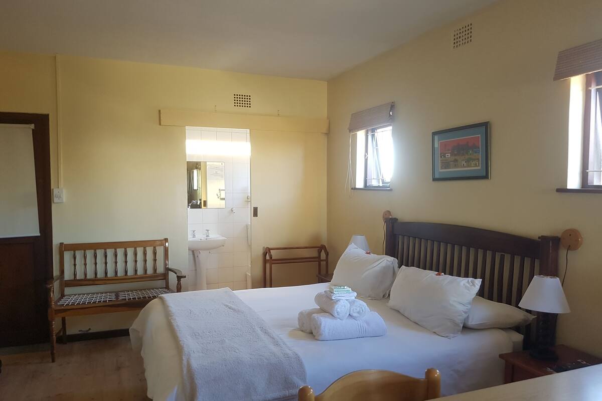 Quarto de hotel com cama, mesa de cabeceira, luminária e um banco.