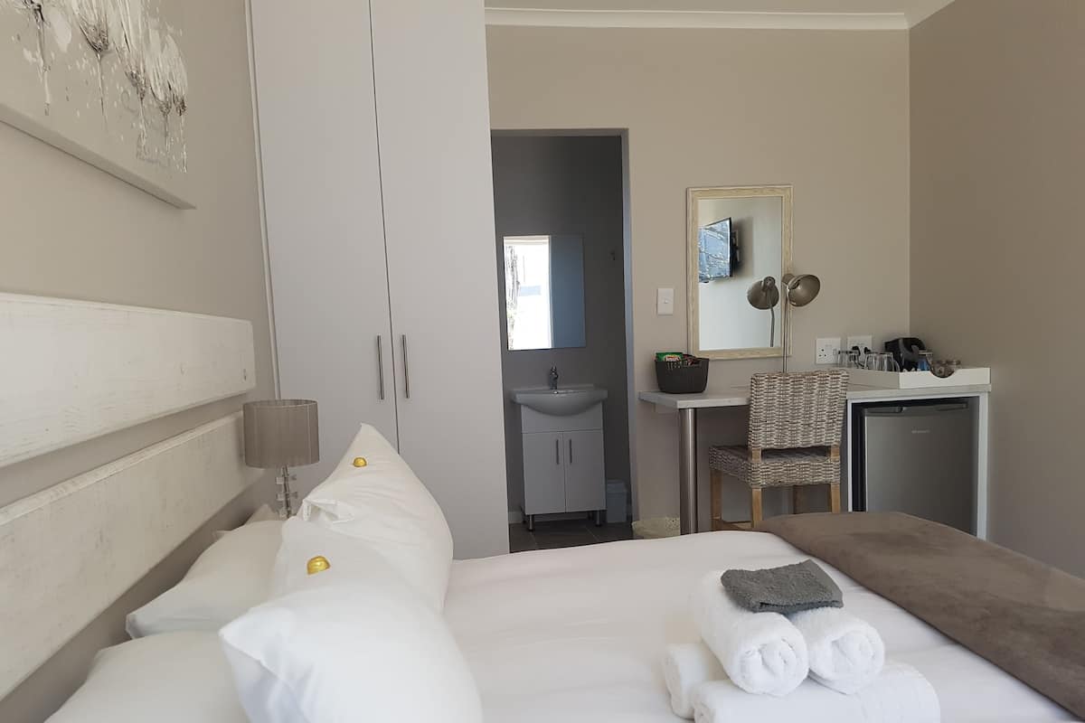 Quarto de hotel com cama, escrivaninha, cadeira, pia e espelho.