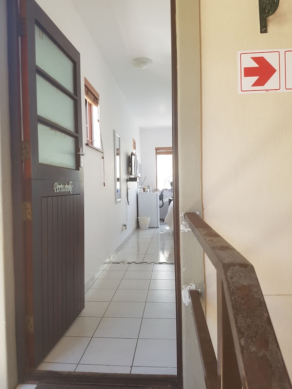 A hallway with a door labeled "Pertamina" leading to a room. A red directional sign is visible on the wall. - Melkbosch Guesthouse (Cape Town)