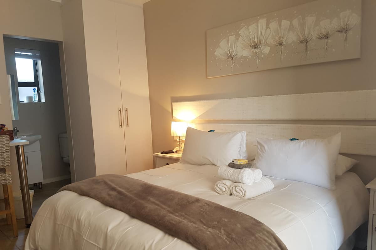 Uma cama bem arrumada com roupa de cama branca e castanha, cabeceira com pintura floral e mesa de cabeceira com abajur e controle remoto.