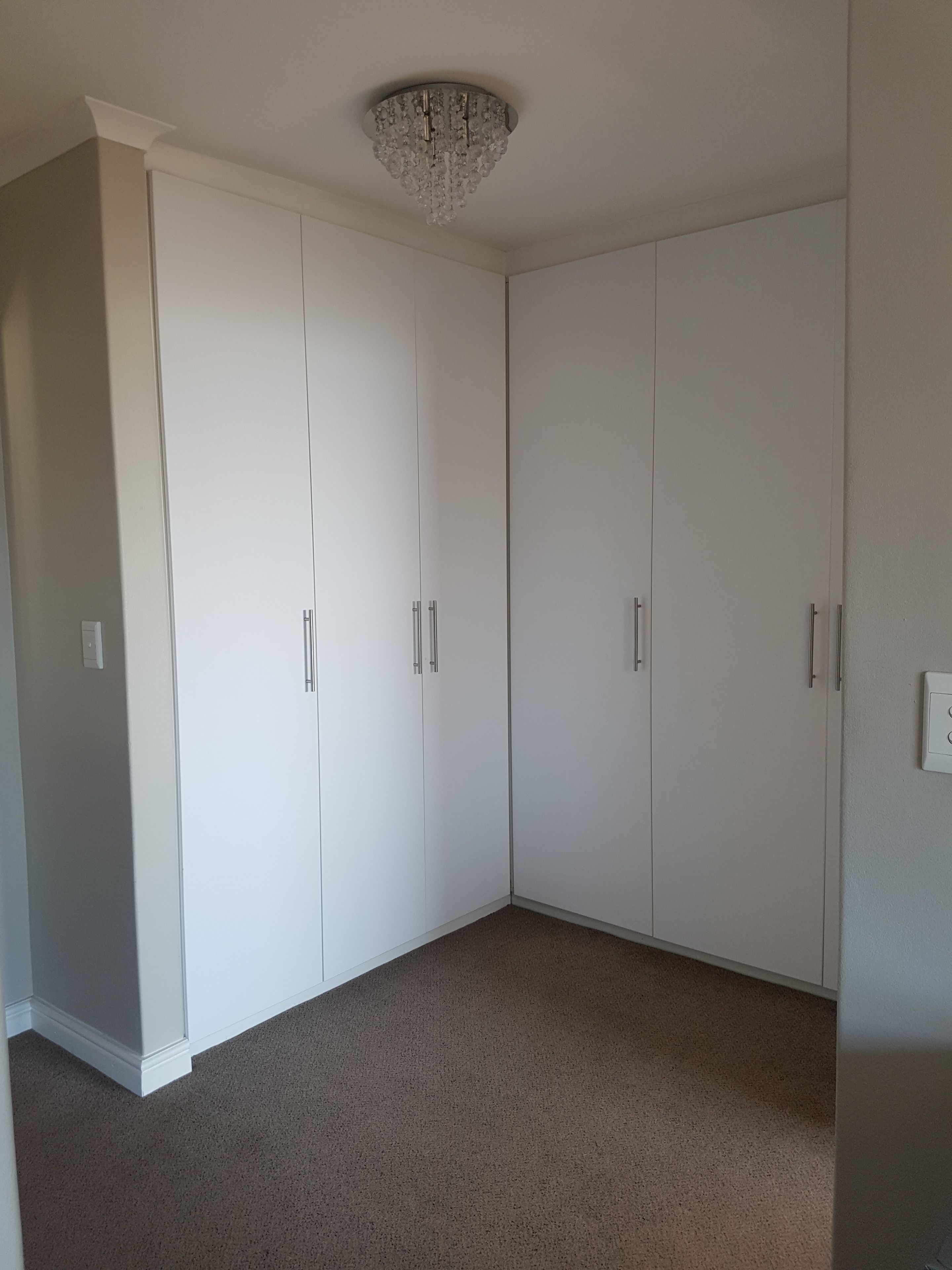 A room with a large white wardrobe, a chandelier, and a carpeted floor.