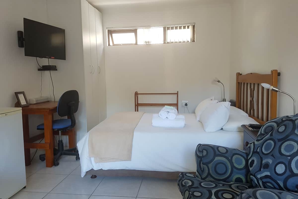 Quarto de hotel com uma cama, uma escrivaninha com cadeira, televisão e janela com cortinas.