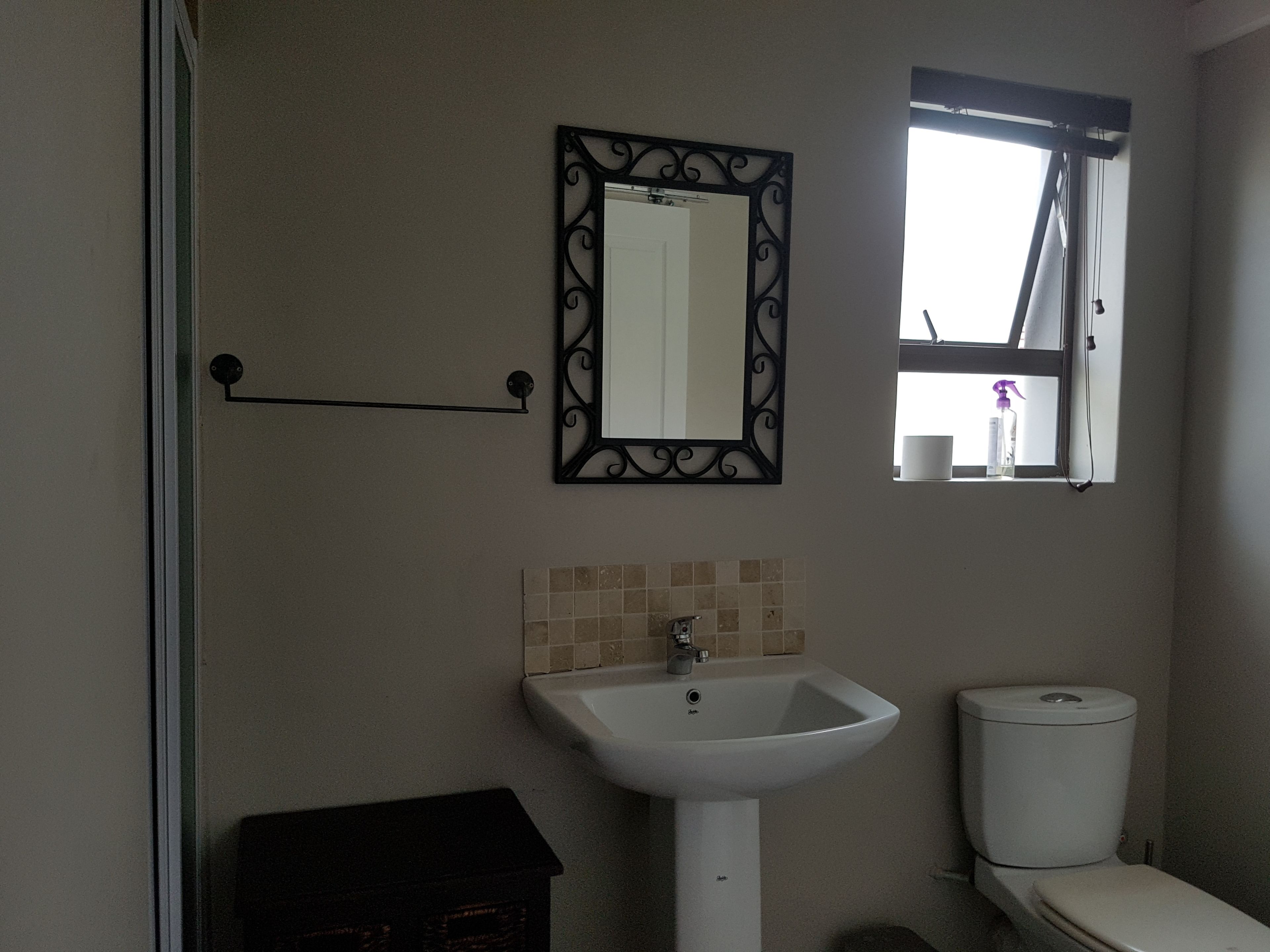 Un baño con lavamanos blanco, inodoro, espejo con marco decorativo y ventana con vistas al exterior.