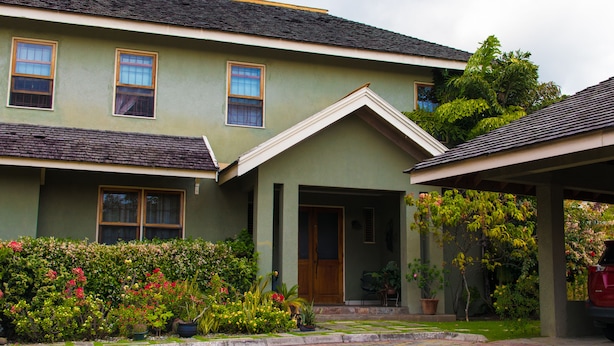 A two-story house with a green facade, a front porch, and a garden with various plants and flowers. - The Inn at 6 (Kingston)