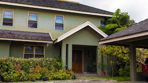 A two-story house with a green facade, a front porch, and a garden with various plants and flowers. - The Inn at 6 (Kingston)