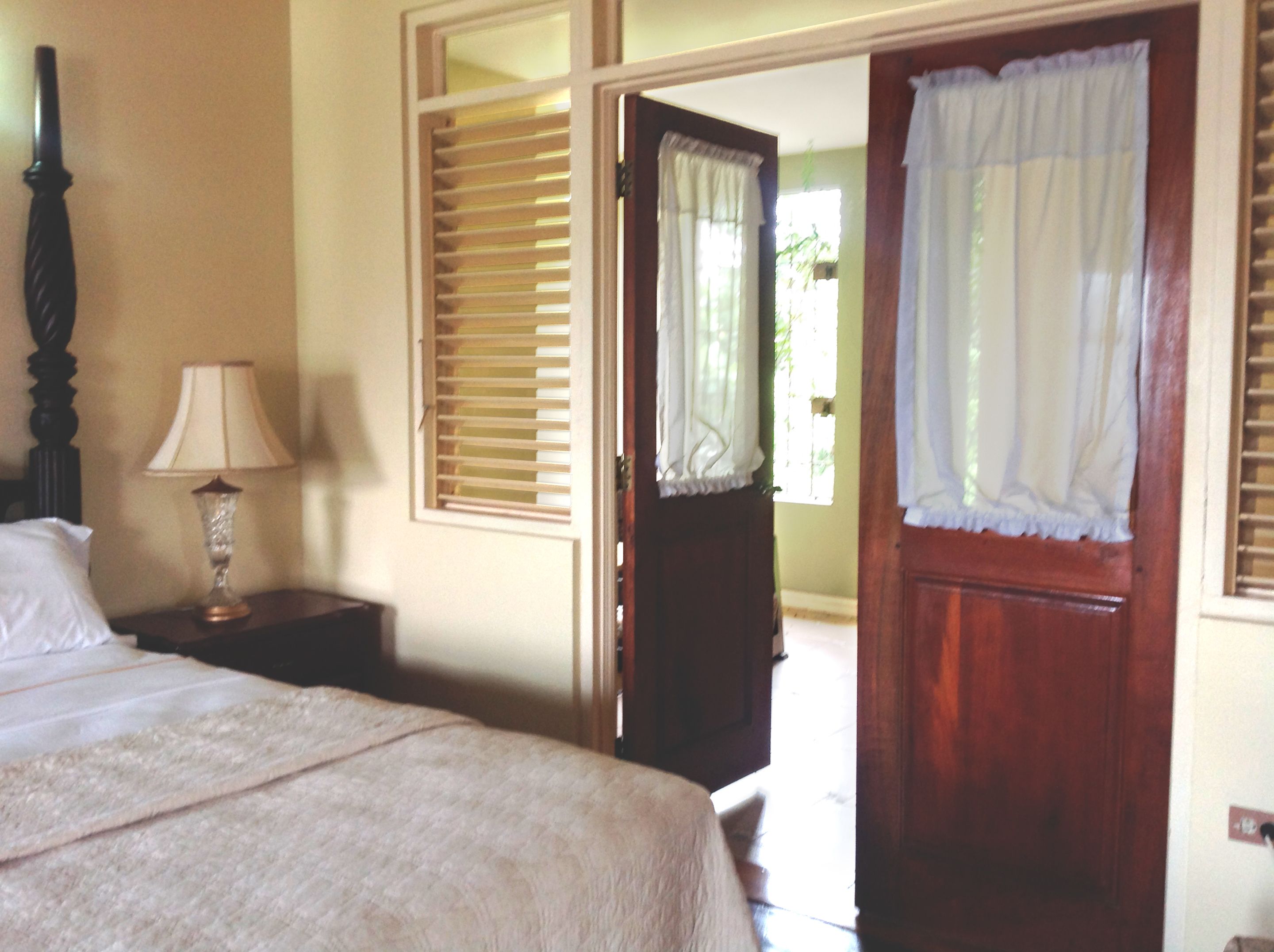 A bedroom with a bed, a nightstand with a lamp, and a door leading to an outdoor area.
