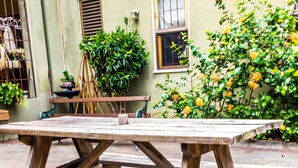 A wooden picnic table in an outdoor courtyard with a brick floor, surrounded by potted plants and a building with windows. - The Inn at 6 (Kingston)