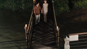 A narrow wooden bridge with railings and candles, surrounded by dense greenery.