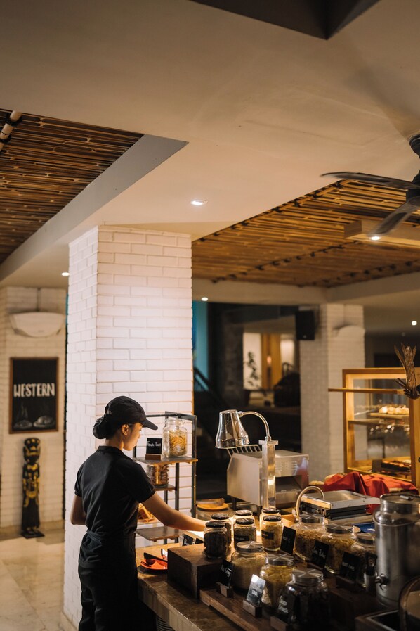 A person working at a counter with various jars and containers, a sign labeled "Western", and a brick wall.