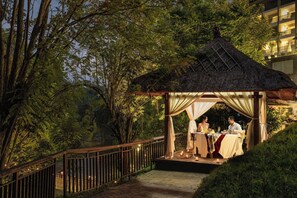 Uma área de refeições ao ar livre com um gazebo, uma mesa posta para dois e um corrimão.