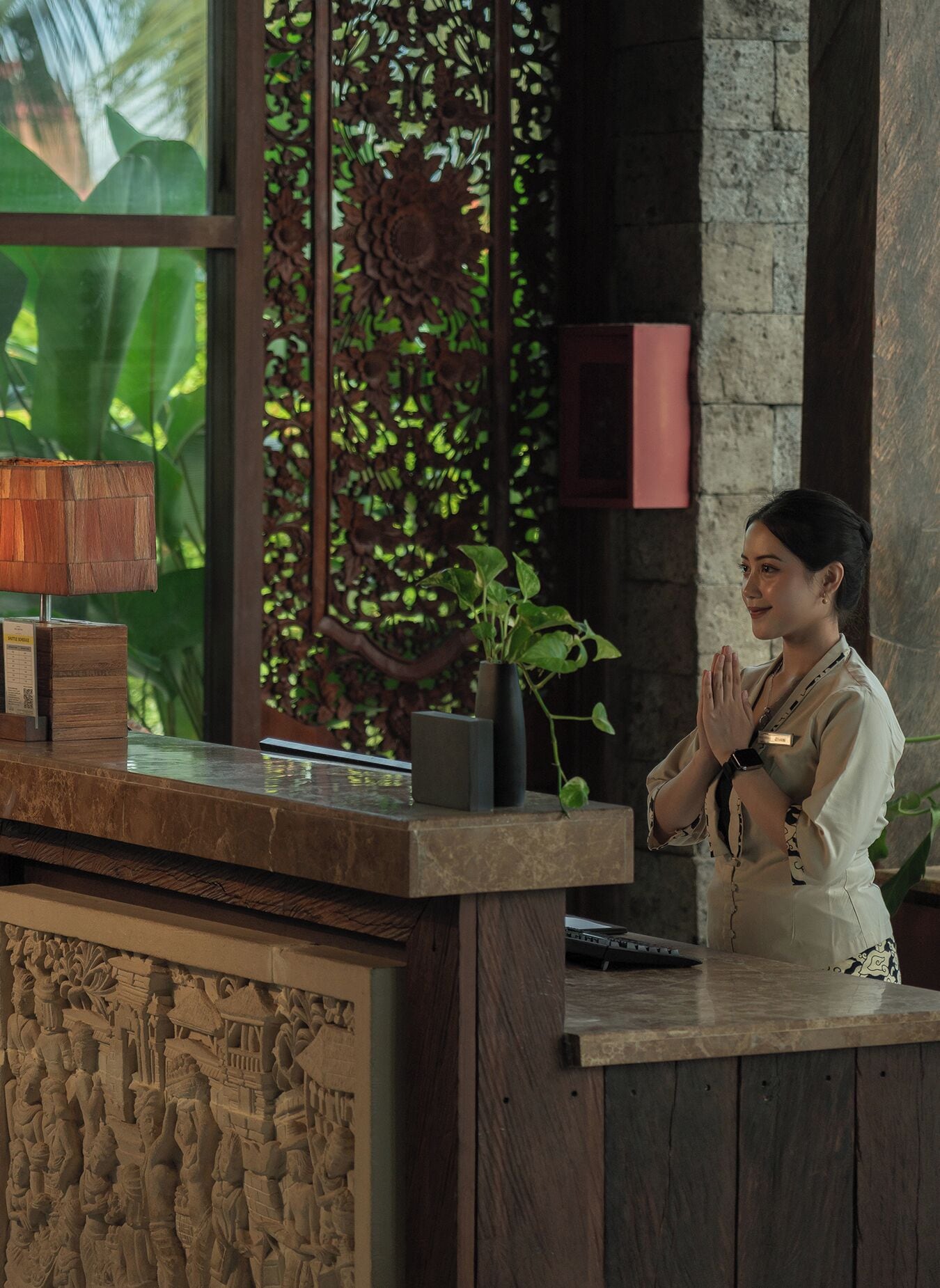 A reception desk with a wooden design, a potted plant, and a decorative panel in the background.