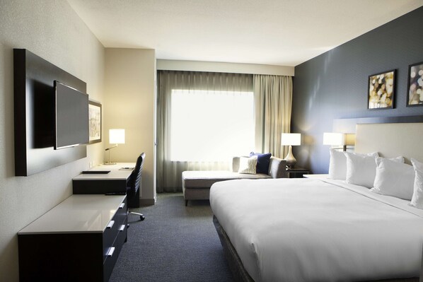 A hotel room with a large bed, a desk with a chair, a flat-screen TV mounted on the wall, and a window with curtains. - Hilton Garden Inn Minneapolis University Area (Minneapolis)