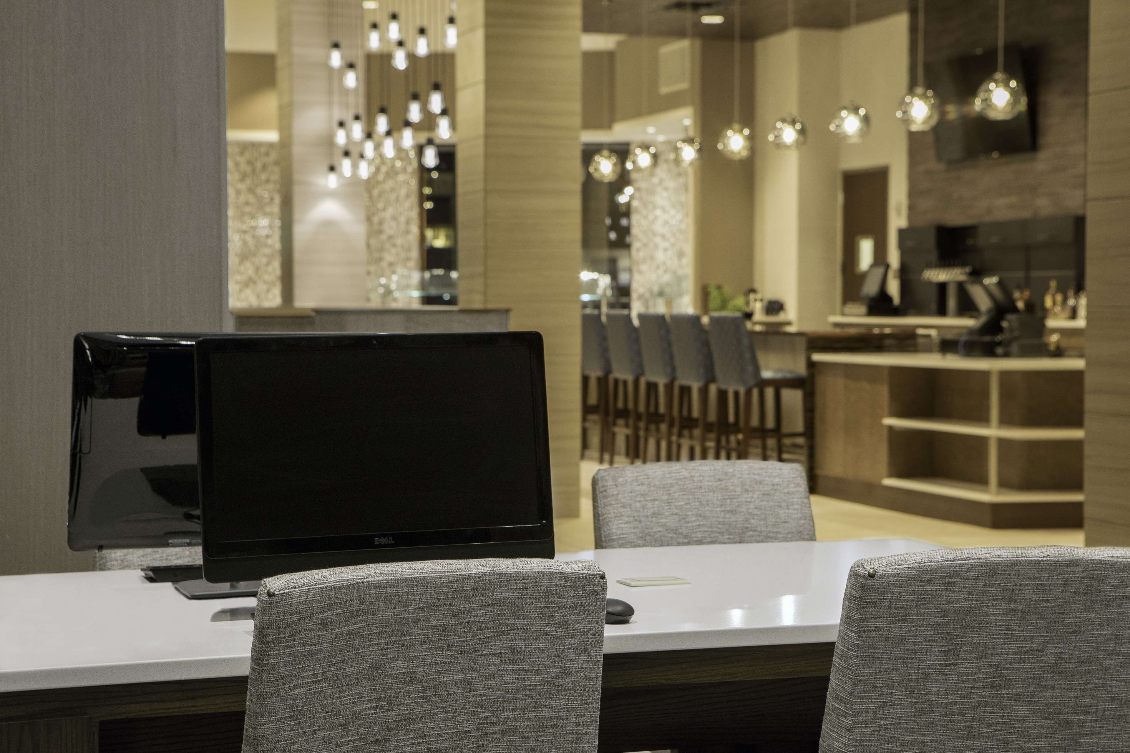 Een moderne eetruimte met een laptop op een tafel, grijs gestoffeerde stoelen en een moderne kroonluchter.
