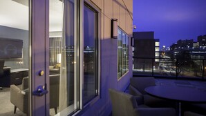 Een moderne hotelkamer met grote ramen, een balkon en uitzicht op de stad 's nachts.