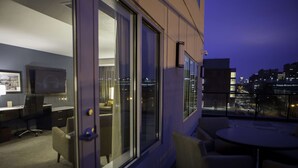 Een moderne hotelkamer met uitzicht op de stad, een bureau met stoel, een bank en een kleine tafel.