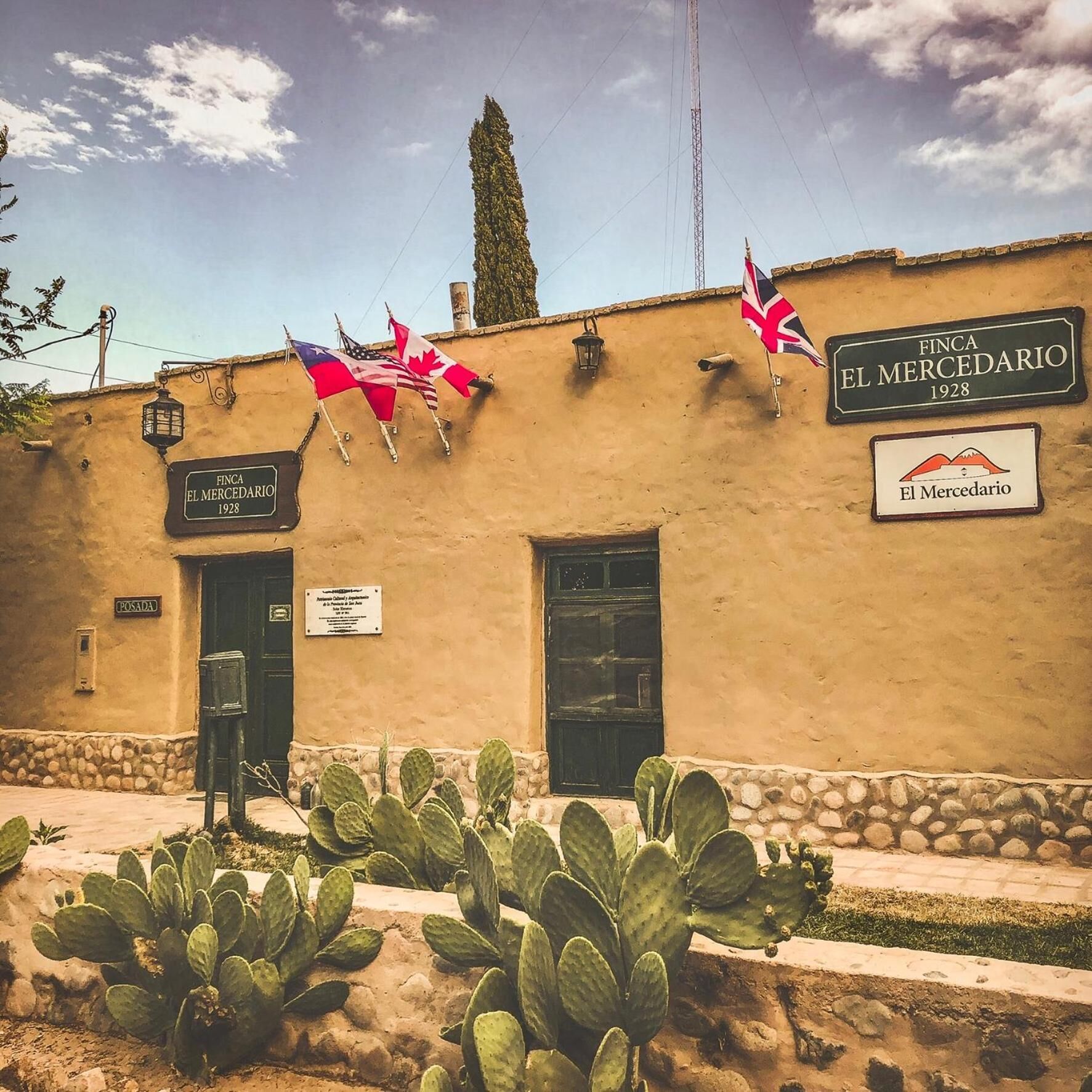 A building with a sign reading "FINCA EL MERCEDARIO 1928" and multiple flags, including the American and Canadian flags.
