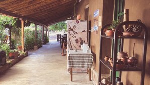 Un espacio al aire libre cubierto con piso de concreto, una mesa con mantel a rayas y repisas con cerámica.