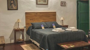 Un dormitorio con cabecera de madera, cama con edredón a rayas, dos mesitas de noche con lámparas, una puerta verde y un cuadro enmarcado en la pared.
