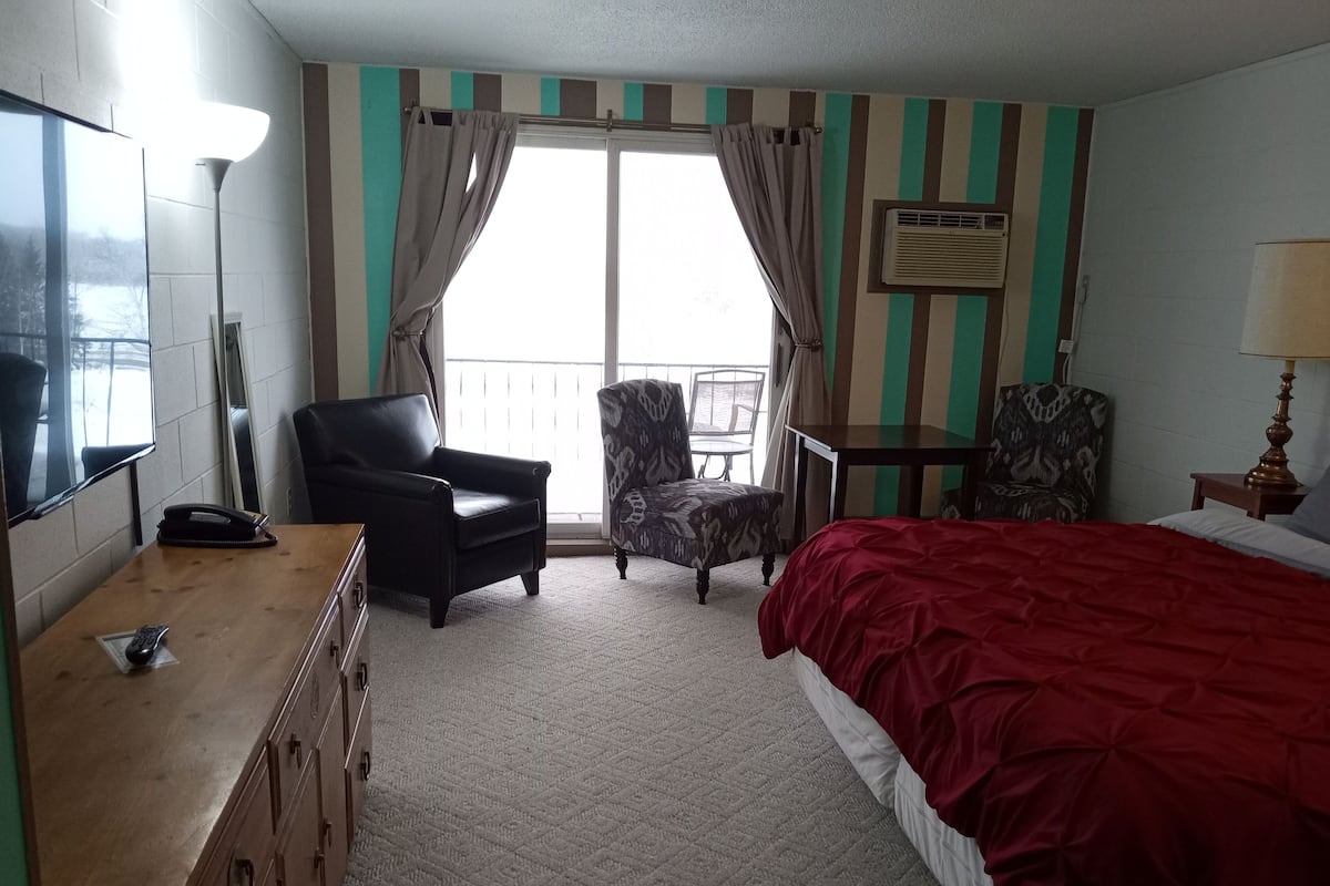 Ein Hotelzimmer mit Bett, Schreibtisch, Stuhl, Fernseher und einem Fenster mit Vorhängen.