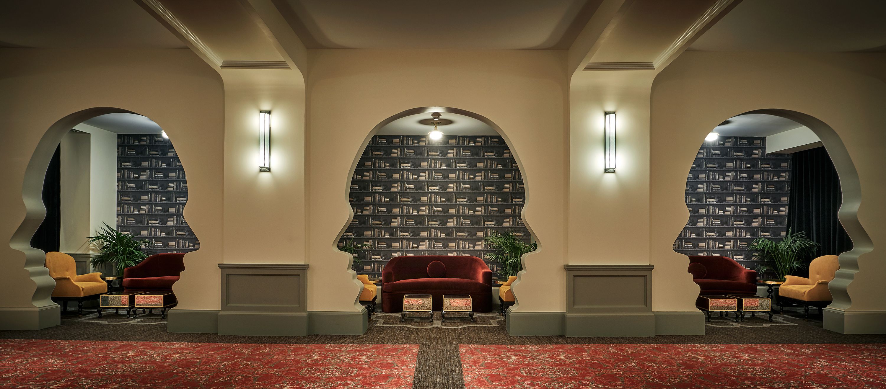 A lobby with a red carpet, two red sofas, yellow armchairs, and a bookshelf in the background.