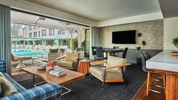 A modern hotel room with a pool view, a dining area, and a living space with a sofa and coffee table.