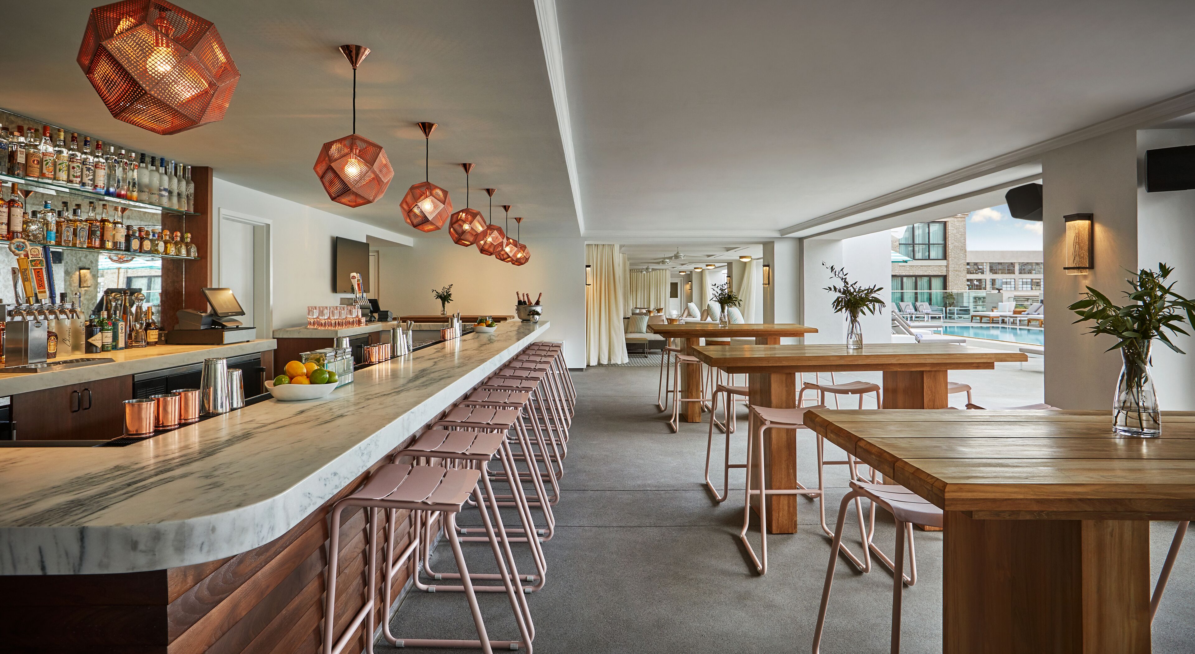 A bar area with a long counter, multiple stools, and copper pendant lighting.