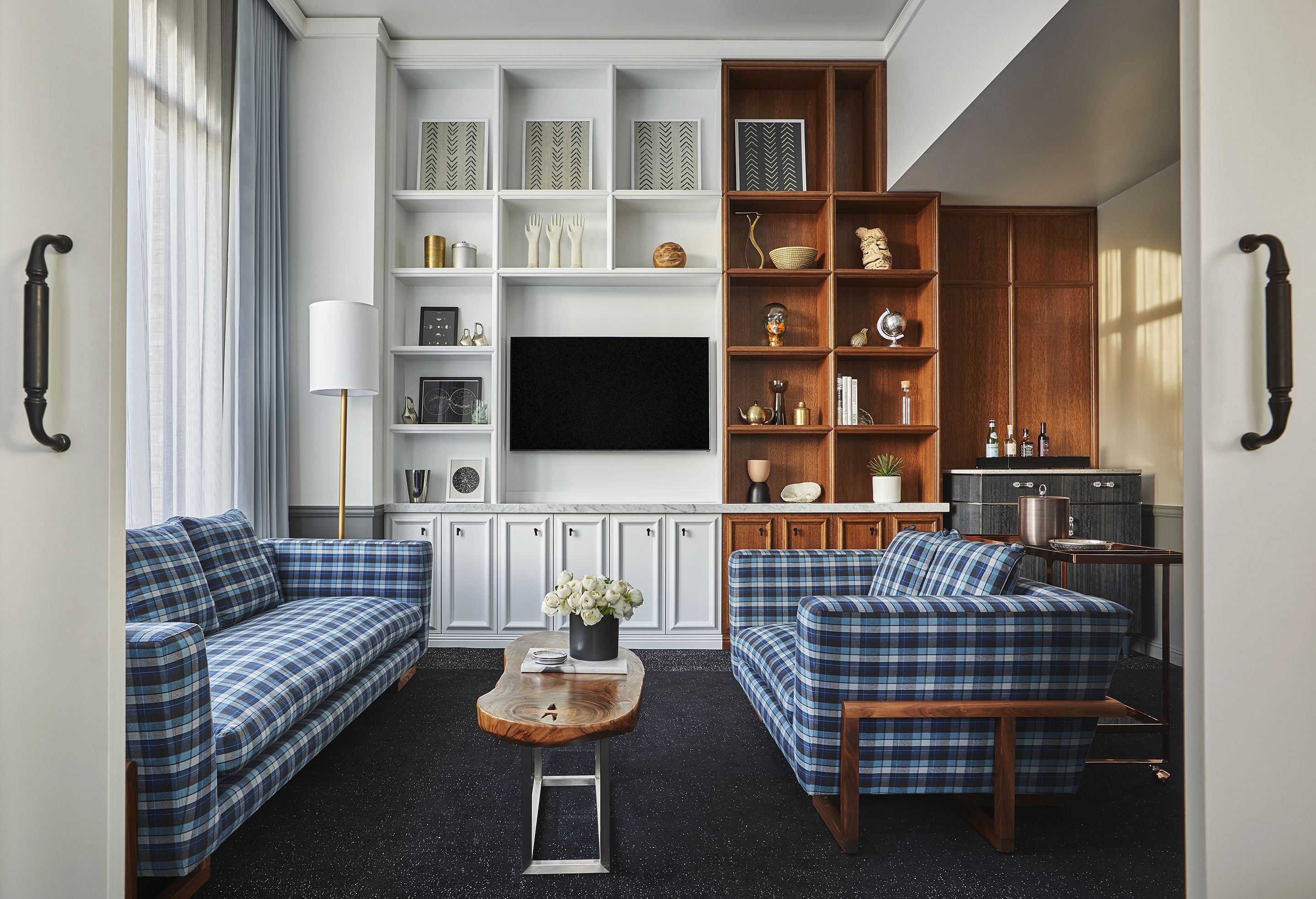 A living room with two blue plaid sofas, a wooden coffee table, and a TV wall unit with shelves.