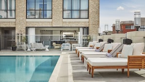 Un área de piscina en la azotea con sillones de descanso y vistas de la fachada de ladrillo del edificio.