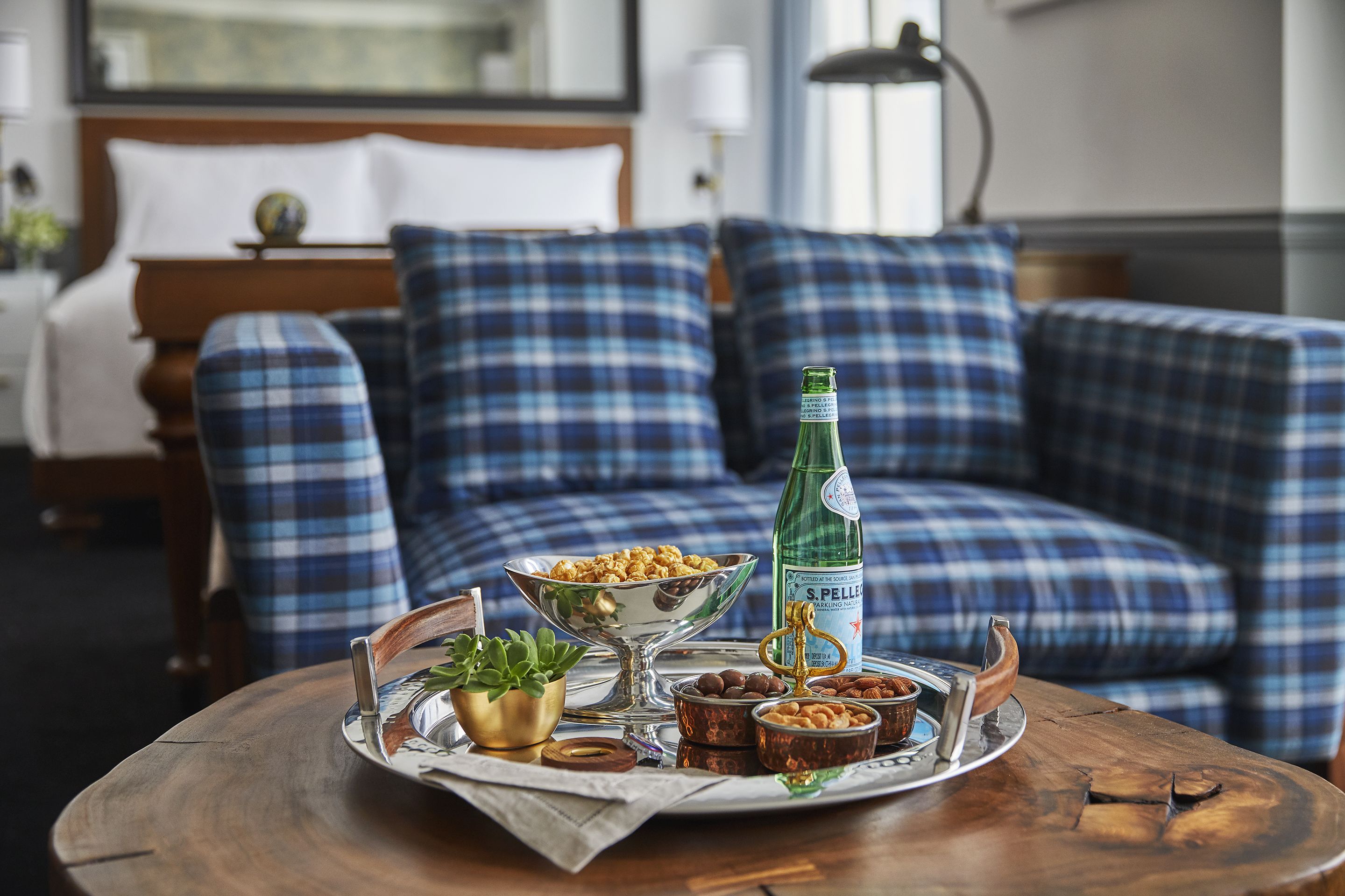 A cozy room with a plaid sofa, a wooden table with snacks, a bottle, and a decorative tray.
