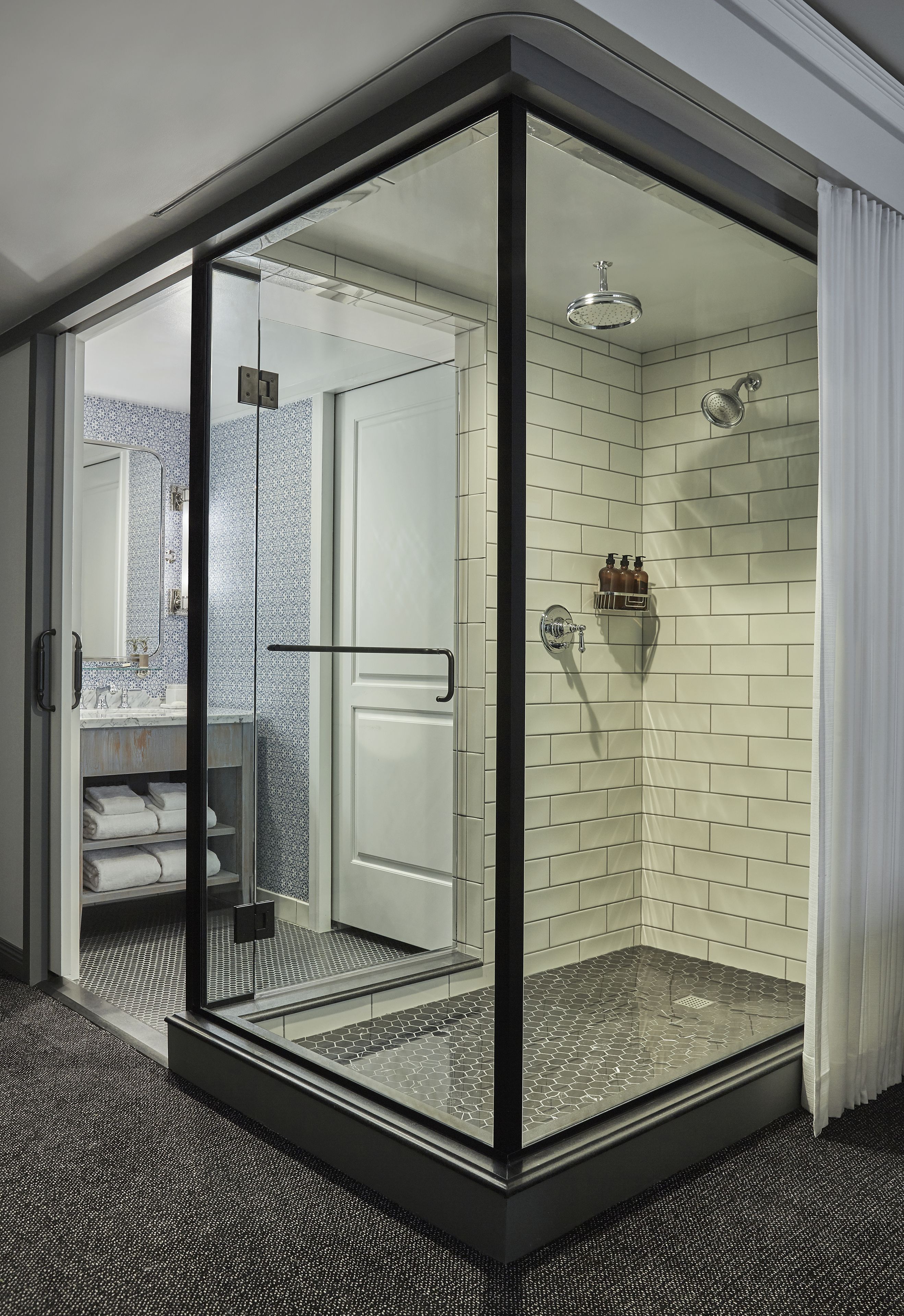 Un baño moderno con ducha de vidrio, paredes de azulejos blancos y un mostrador visible con toallas.