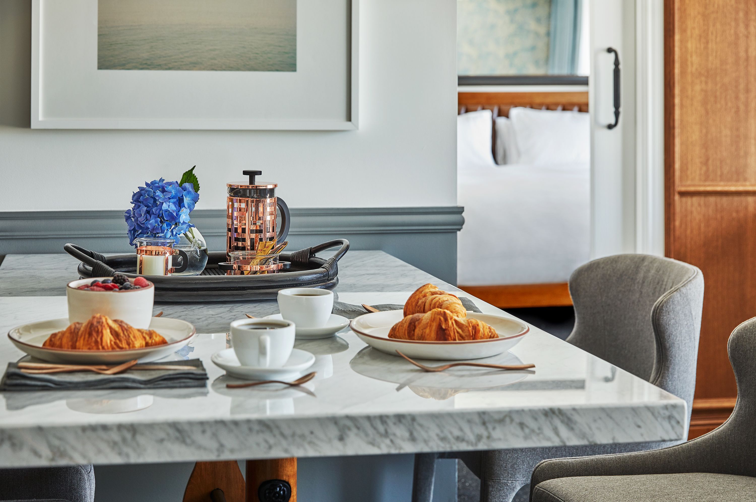 A breakfast setting with croissants, coffee, and a fruit bowl on a marble table.